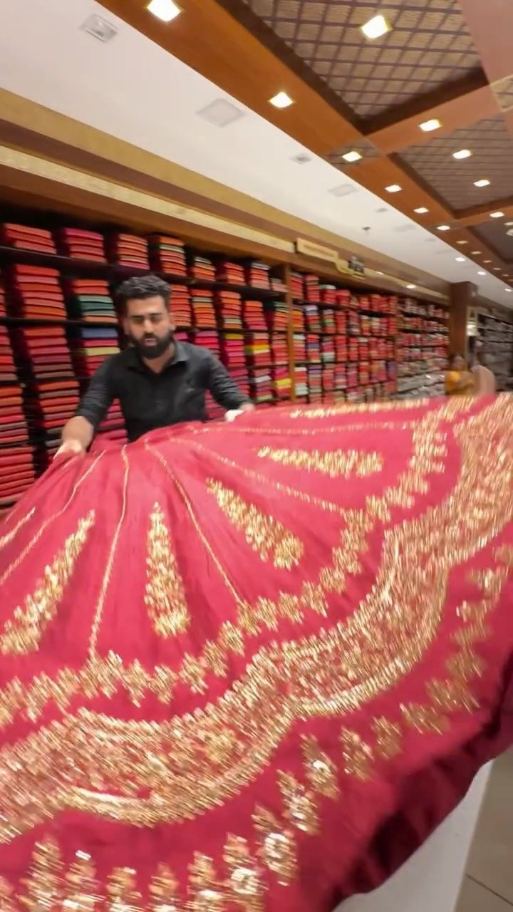 Kasavu Kendra staff presenting a gold-bordered bridal saree against the wall of stacked silks
